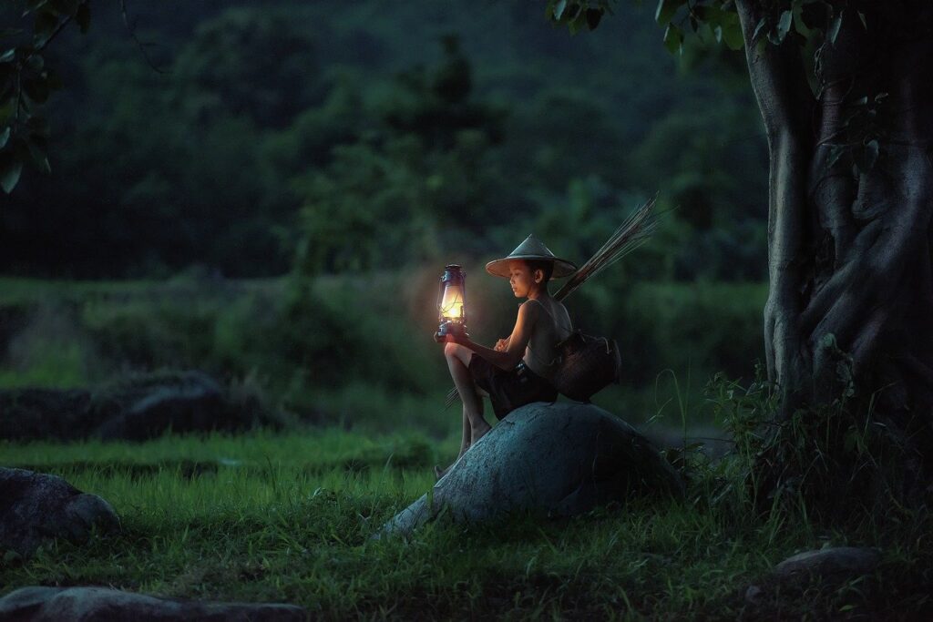 Boy with lantern and fishing rod sitting on rock at night